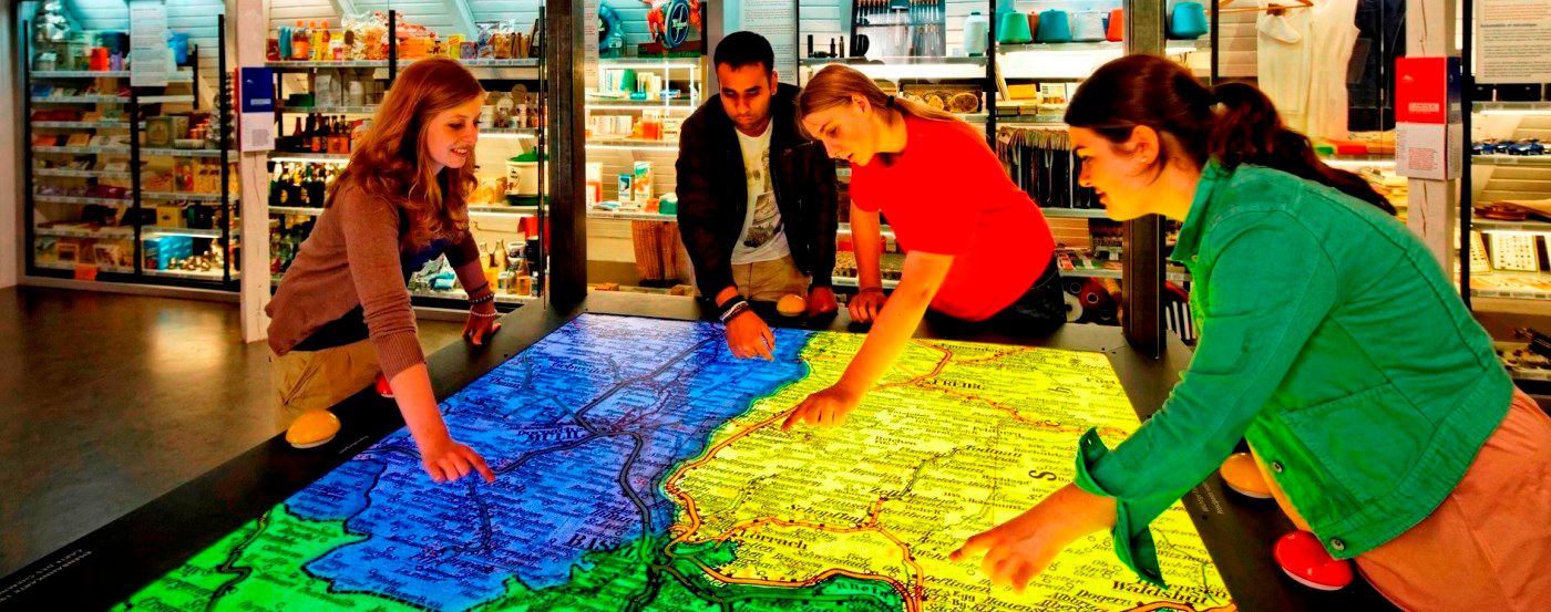 Vier Personen erkunden interessiert eine beleuchtete Karte auf einem grossen Tisch im Museum