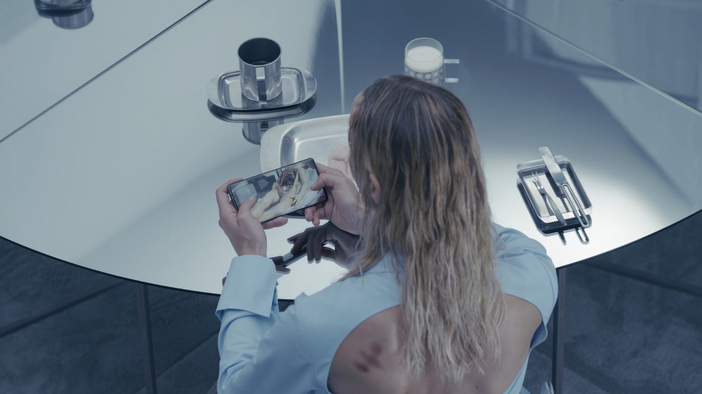 A person with an open back views something on their smartphone at a reflective table