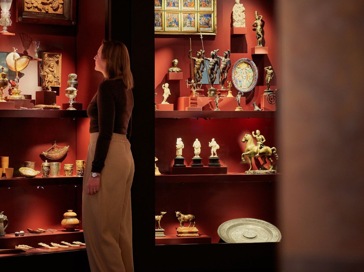 Eine Frau betrachtet in einem Museum sorgfältig eine Vitrine voller kunstvoller antiker Objekte