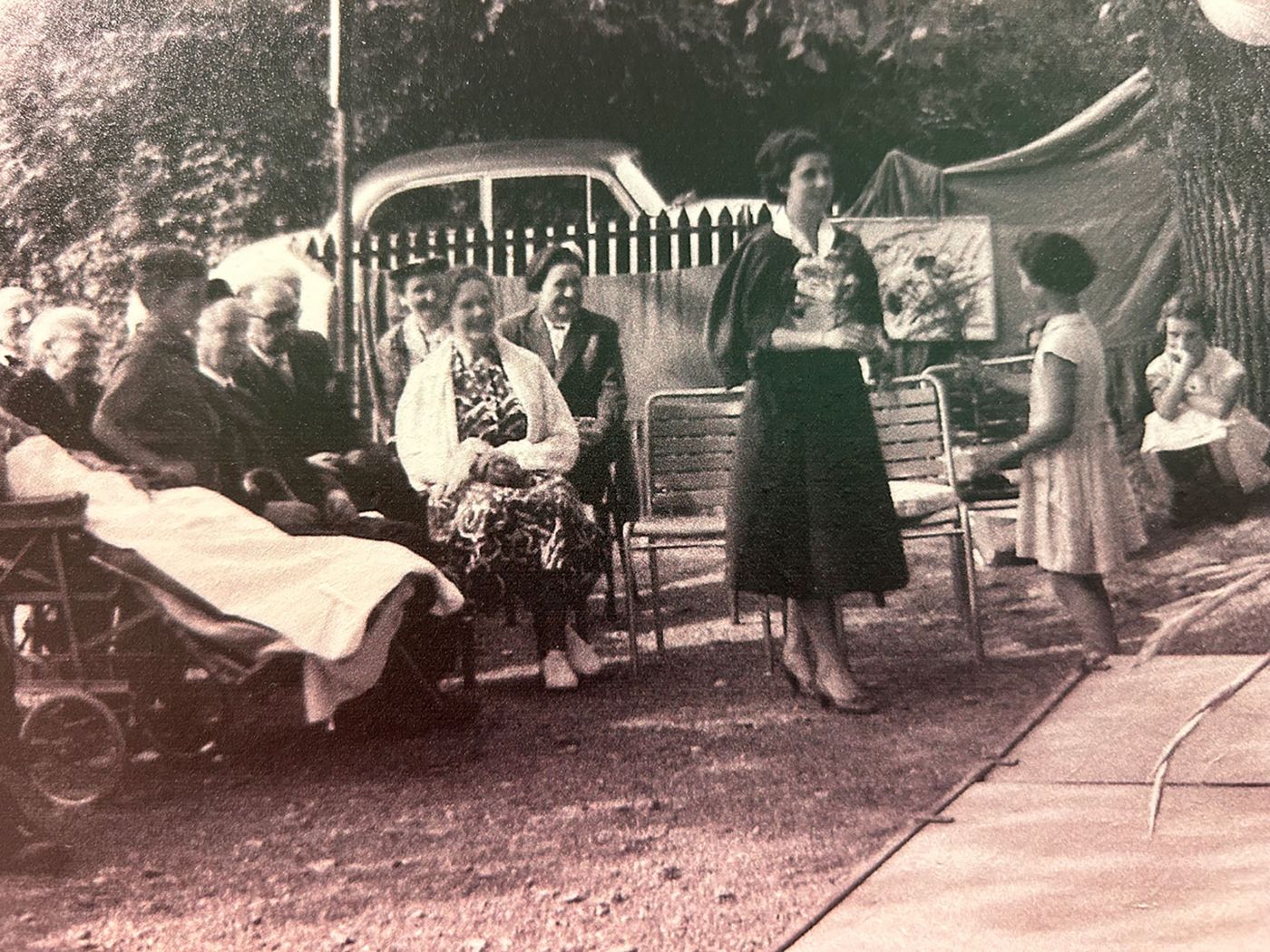 Altes Schwarzweissfoto von Menschen die draussen gemeinschaftlich auf Bänken sitzen.
