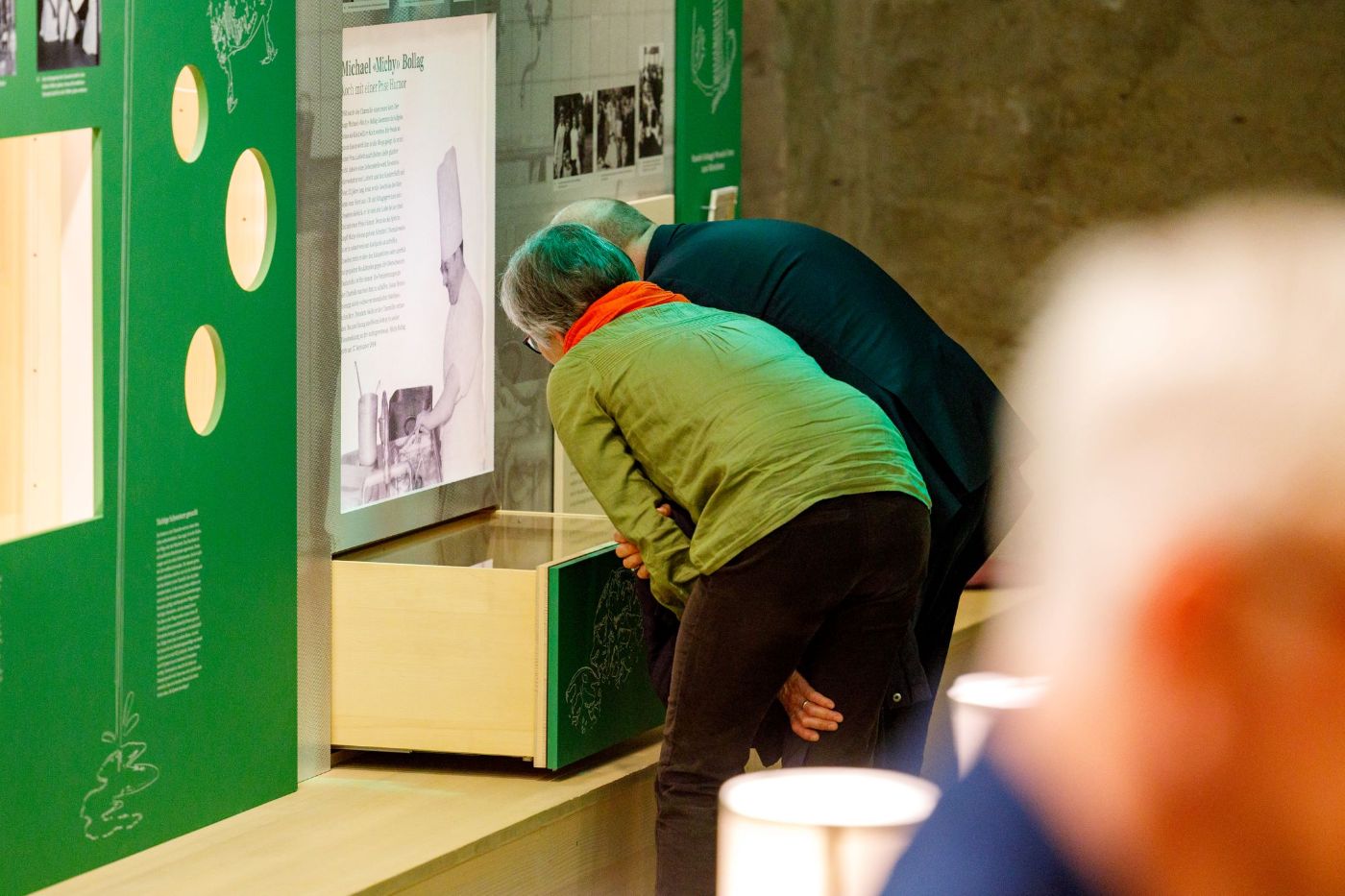Zwei Personen betrachten eine Info-Tafel und eine Schublade in der Ausstellung "Schabbes, Schnitzel, Mehrbettzimmer"