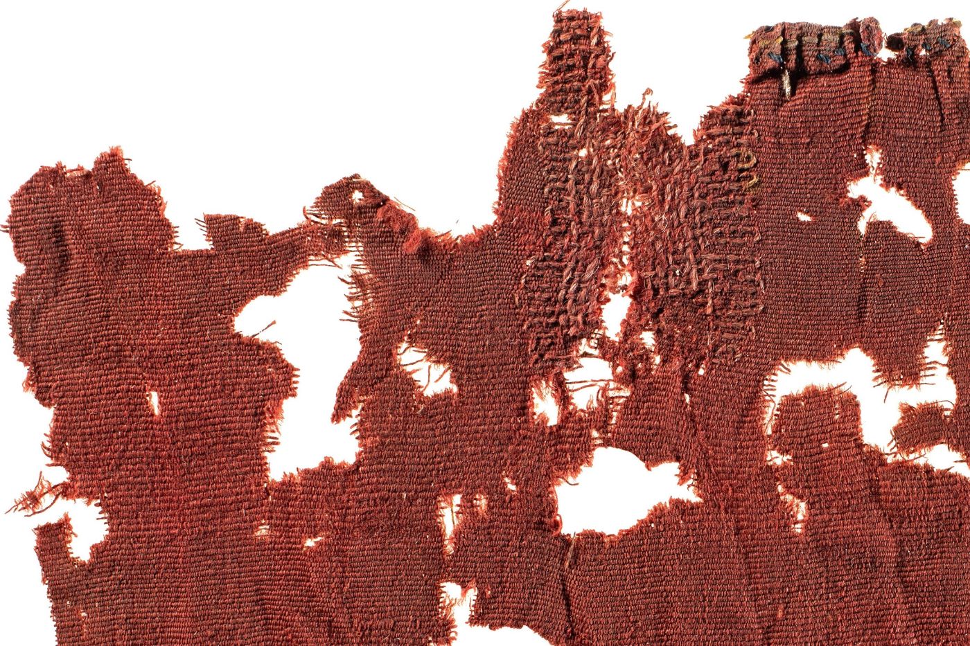 Ein altes, rotbraunes Stofffragment zeigt Spuren von Abnutzung und kunstvoller Reparatur