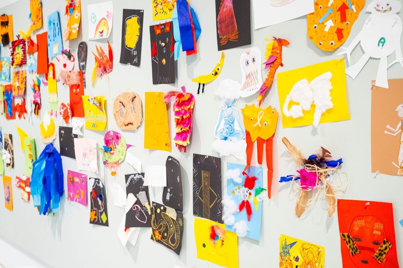 Eine bunte Wand mit vielfältigen, kreativen Kunstwerken, darunter Zeichnungen und Collagen