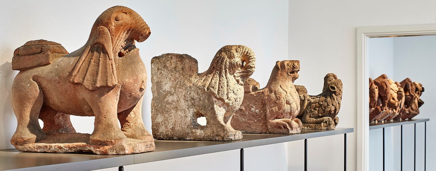 Eine Reihe mittelalterlicher steinerner Löwenfiguren steht auf einem Regal in einem Ausstellungsraum
