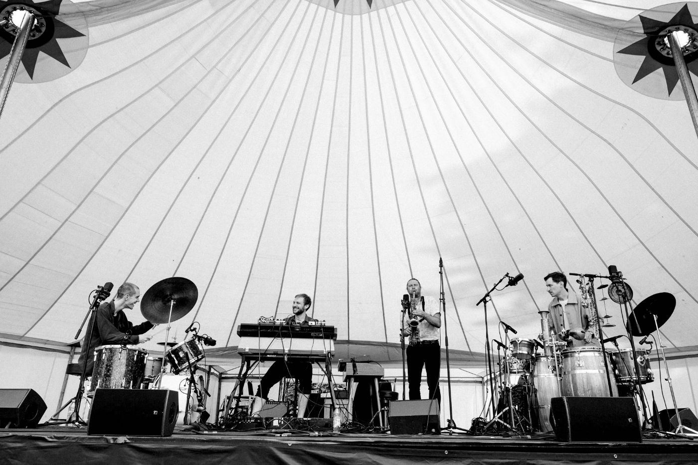 Vier Musiker spielen lebhaft unter einem grossen Festzelt mit Schlagzeug, Keyboard und Saxophon.