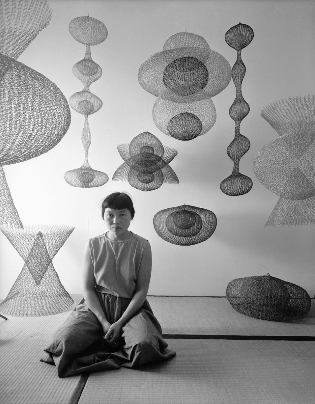 Künstlerin Ruth Asawa kniet inmitten mehrerer ihrer Skulpturen
