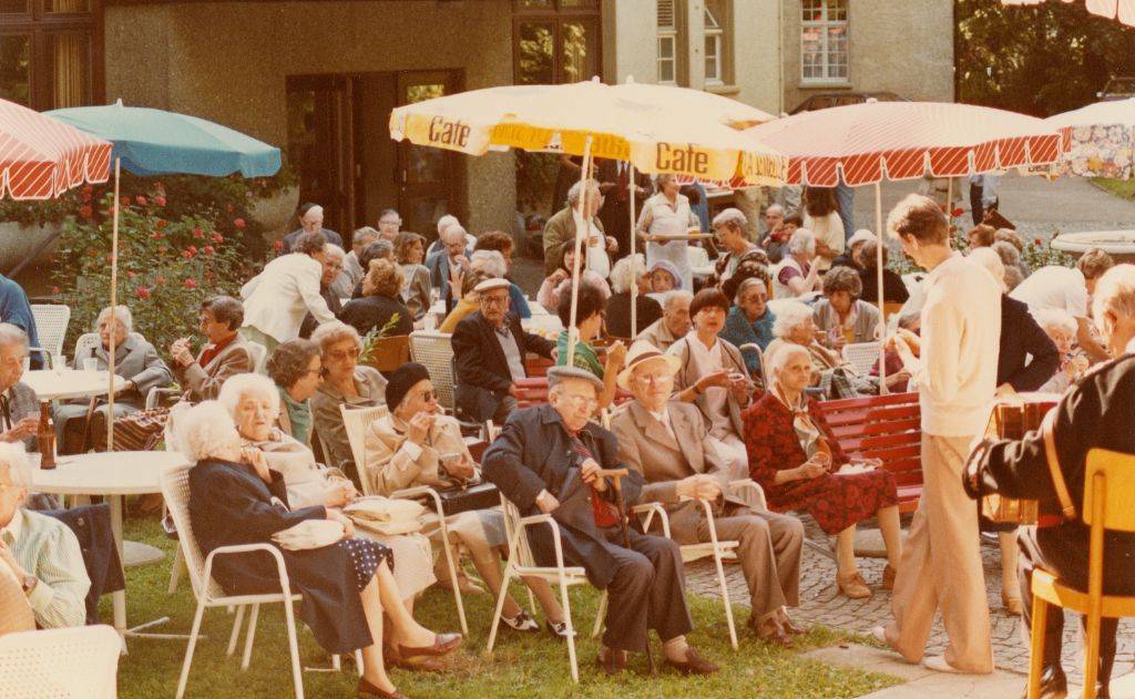 Eine Gruppe von älteren Menschen sitzt im Freien unter bunten Sonnenschirmen und unterhält sich
