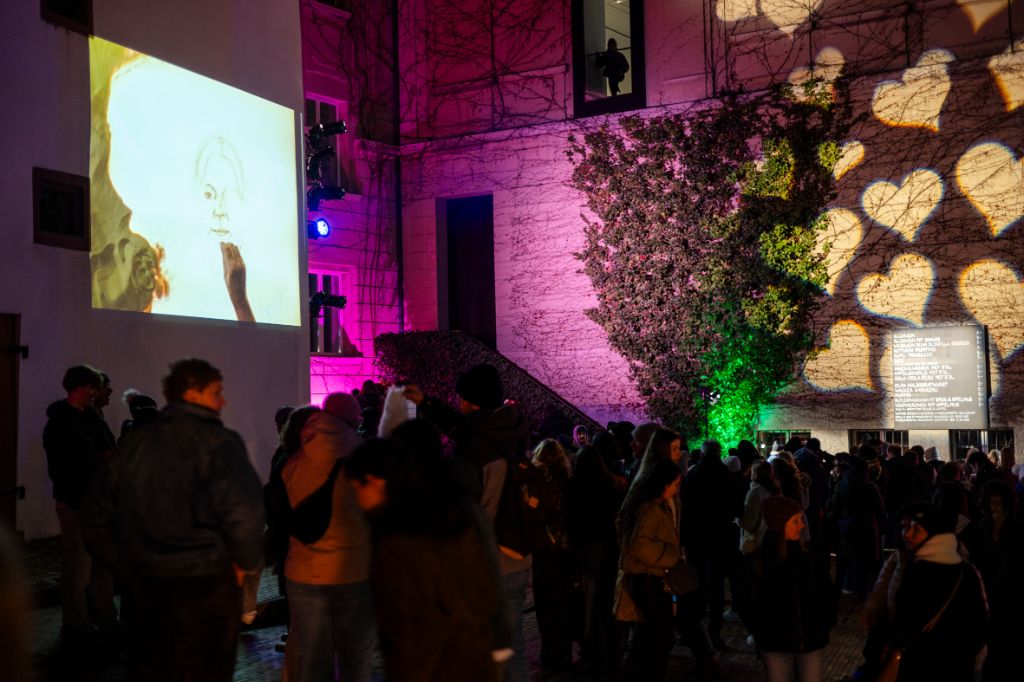 A colorful wall projection shows a drawn face before a crowd at night