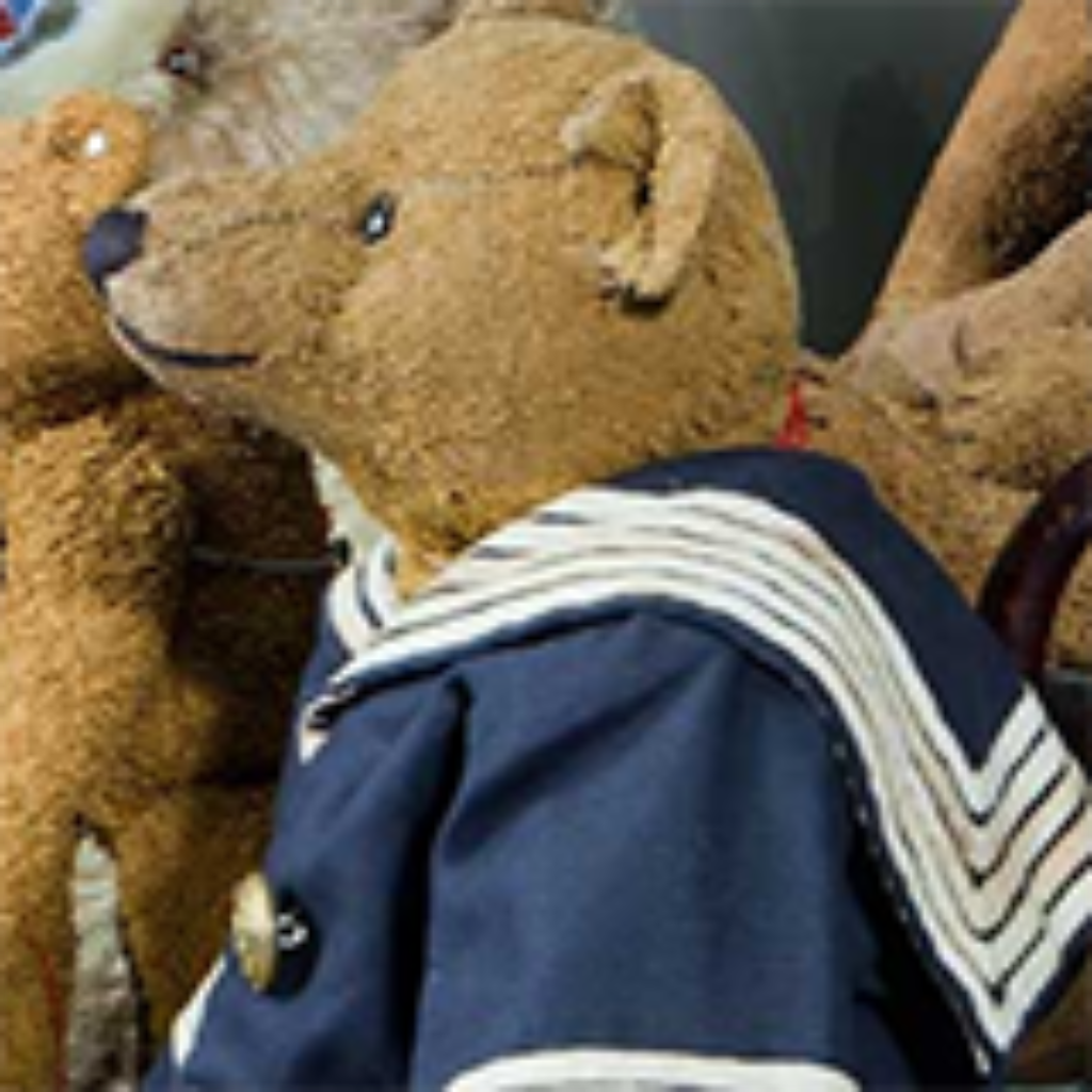 A teddy bear in a sailor suit sits among other plush toys.