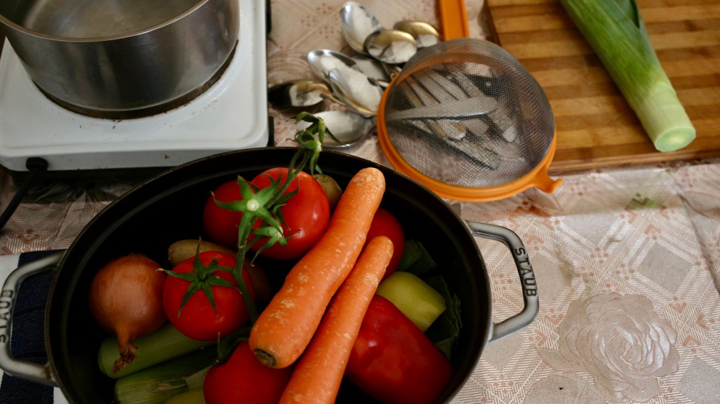 Ein Topf mit frischem Gemüse wie Karotten und Tomaten steht neben einem Herd auf einem Tisch. 