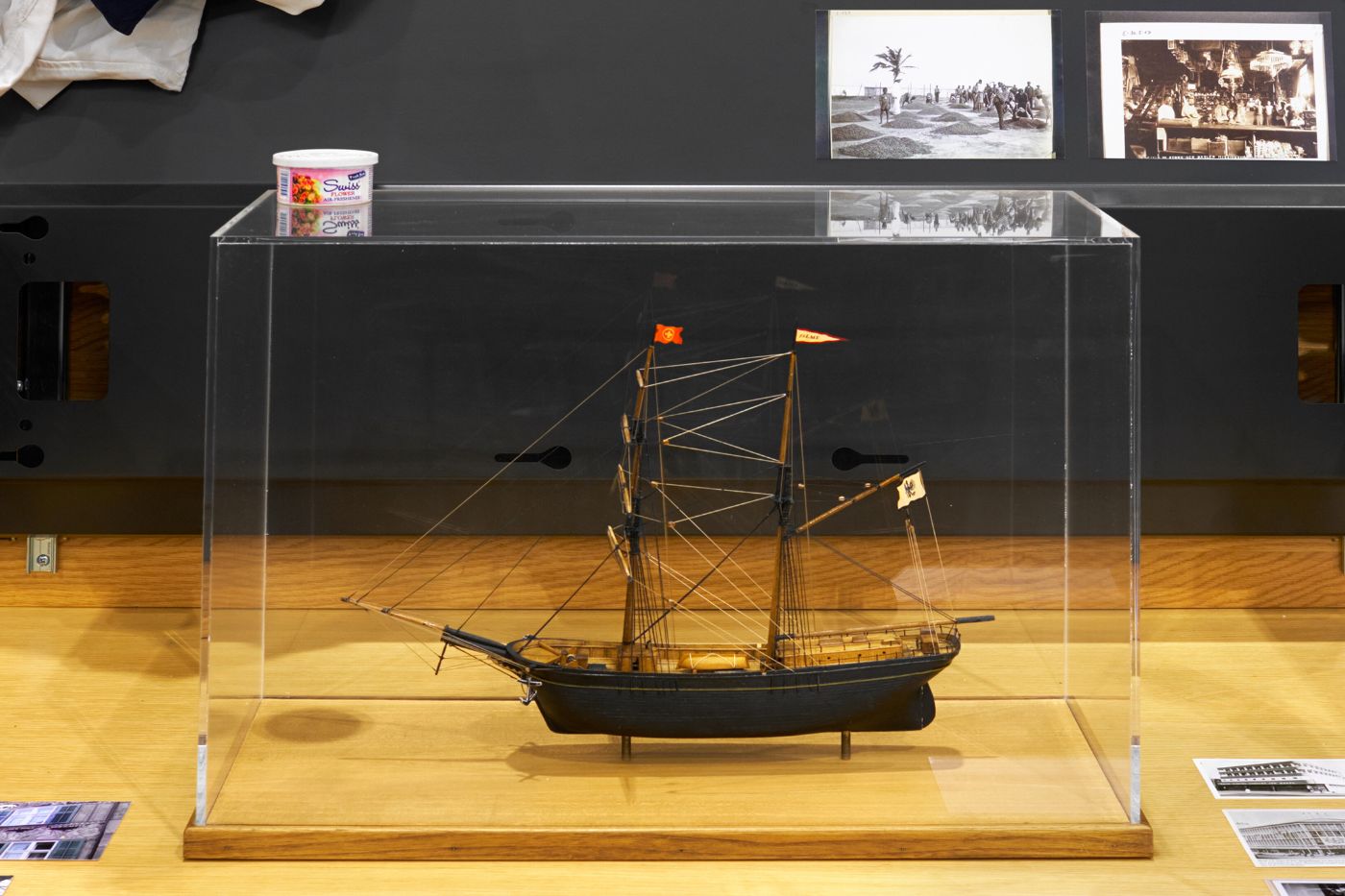 Ein detailliertes Schiffsmodell in einer Glasvitrine, umgeben von historischen Fotos und Objekten