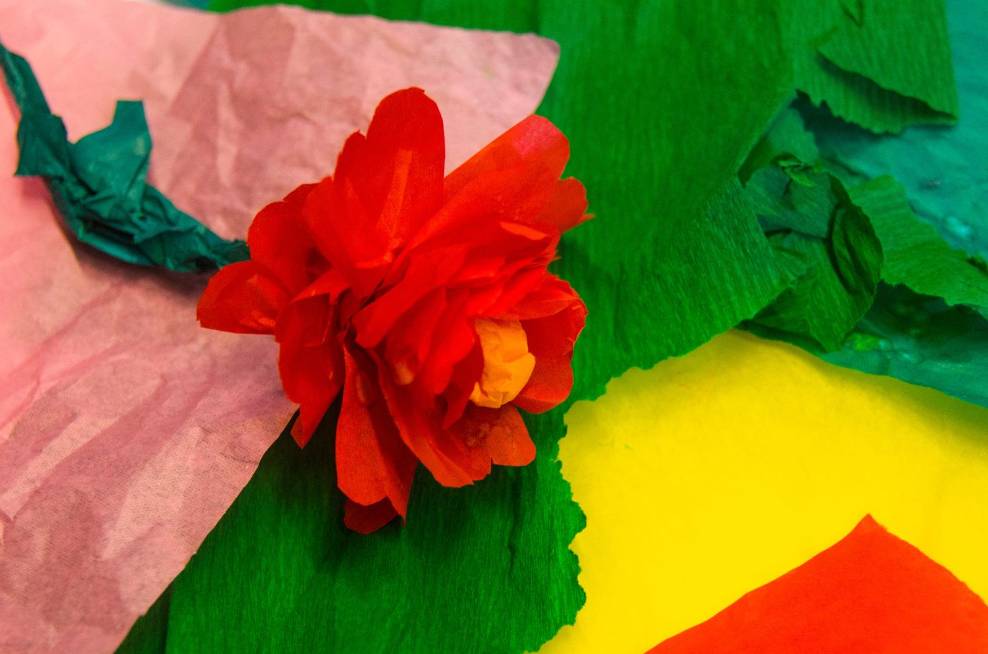 Eine leuchtend rote Papierblume liegt auf bunten Krepppapierbögen in verschiedenen Farben