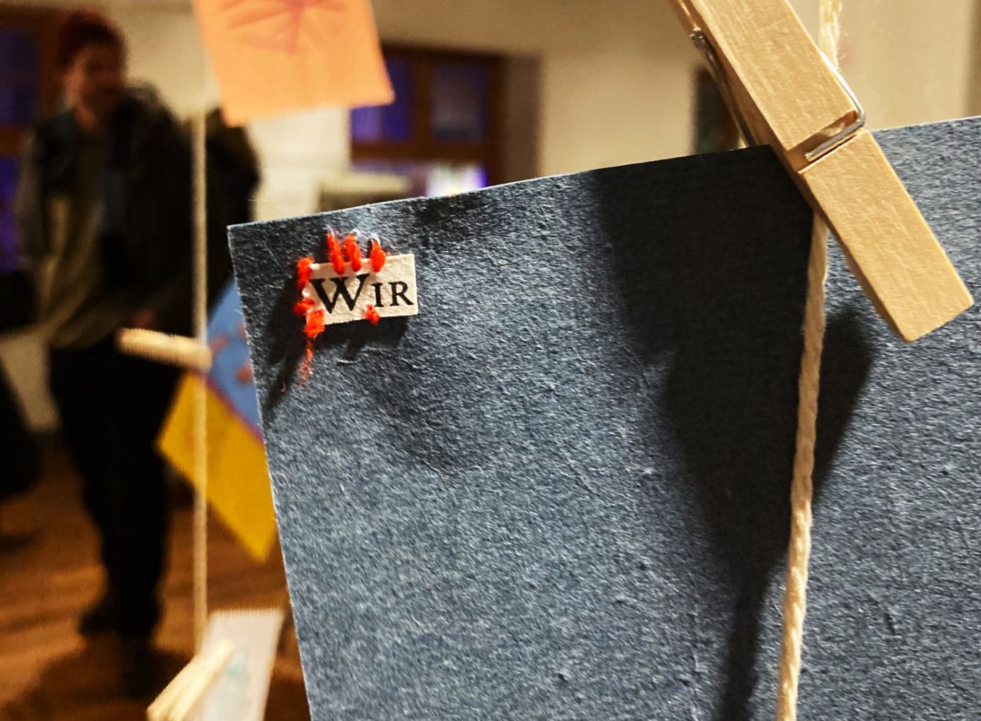 Eine dunkelblaue Karte ist an einer Schnur mit einer Holzklammer befestigt, mit roter Stickerei verziert.
