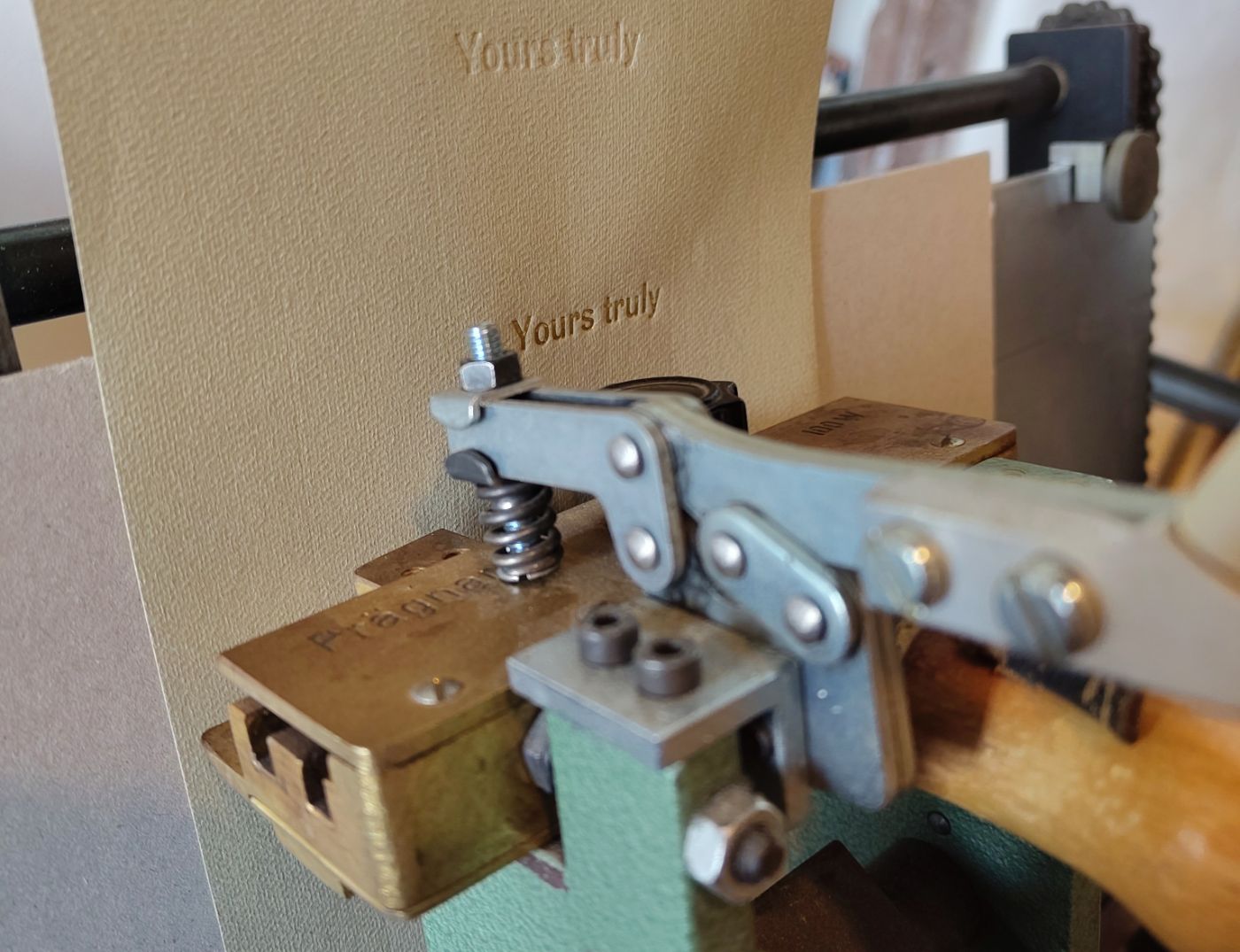 Eine Metallpresse prägt die Worte "Yours truly" in ein sandfarbenes Papier ein.