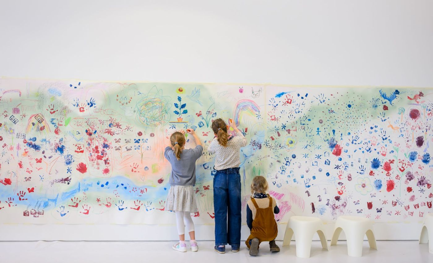 Drei Kinder gestalten gemeinsam ein grosses, buntes Wandbild mit verschiedenen Farben und Mustern