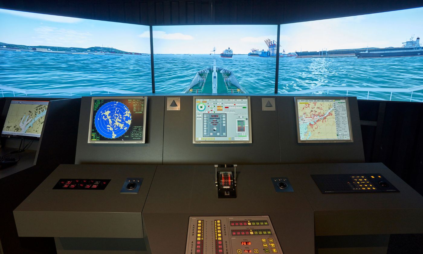 A realistic ship simulator console with multiple screens and control levers in front of a three-panel sea projection.