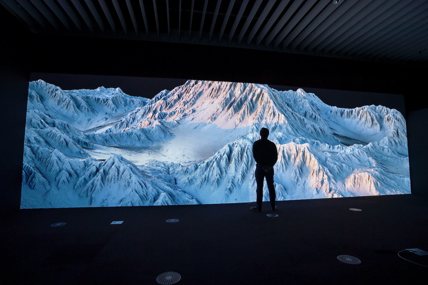 Eine Person betrachtet eine grosse, digitale Berglandschaft, die auf einem Bildschirm projiziert wird