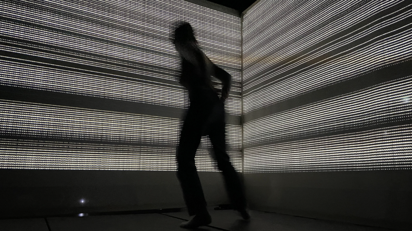 Eine Person bewegt sich vor einem Hintergrund aus horizontalen, leuchtenden Streifen