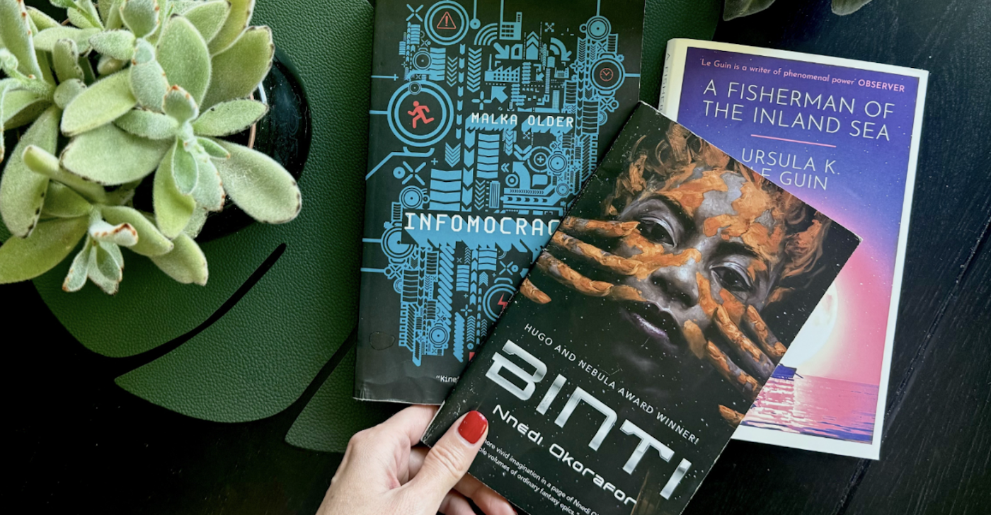 Eine Hand mit rotem Nagellack hält das Buch "Binti" neben zwei anderen Sci-Fi-Büchern.