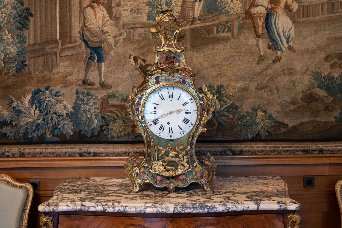 Eine reich verzierte antike Uhr steht auf einem Marmortisch vor einem Wandteppich