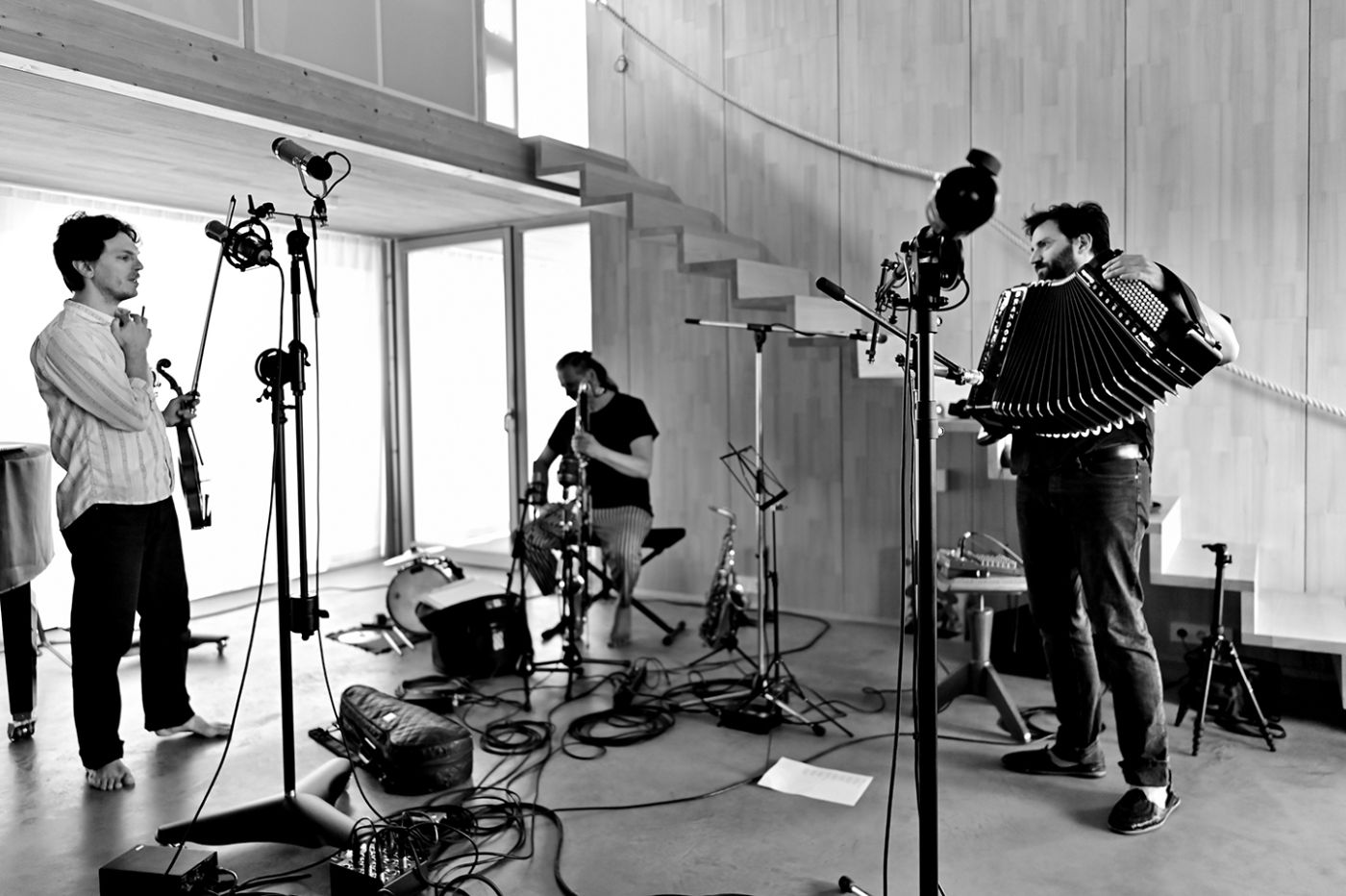 Drei Musiker proben in einem modernen Raum mit einem Kontrabass, Akkordeon und Mikrofonen