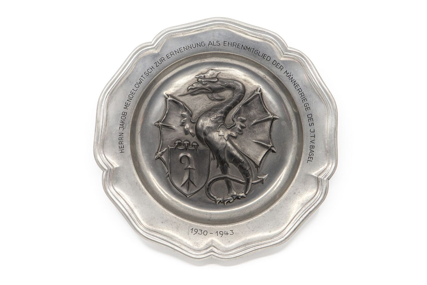 Eine silberne Plakette zeigt einen detailreichen Drachen, umgeben von einer eingravierten Widmung