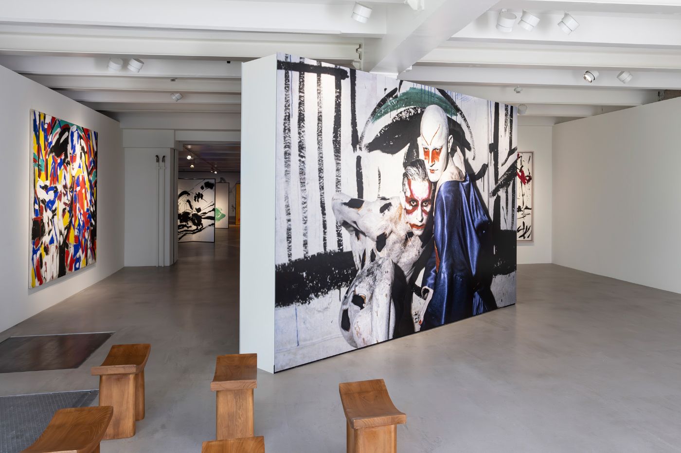 A gallery displays colorful and monochrome artworks with minimalist wooden benches in the foreground