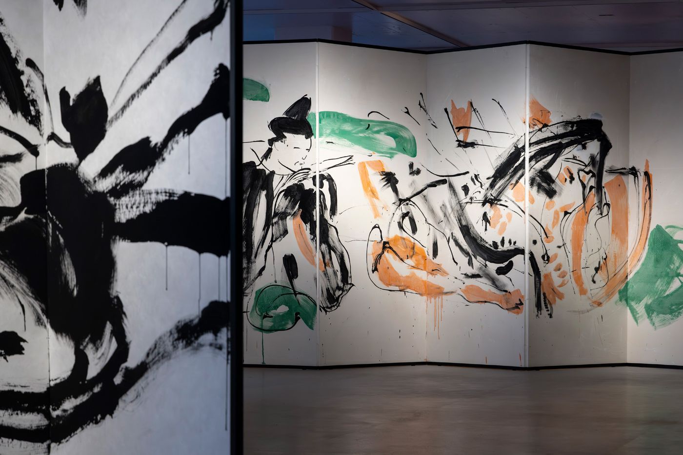 A room with large panels displays bold black brushstrokes on a light background