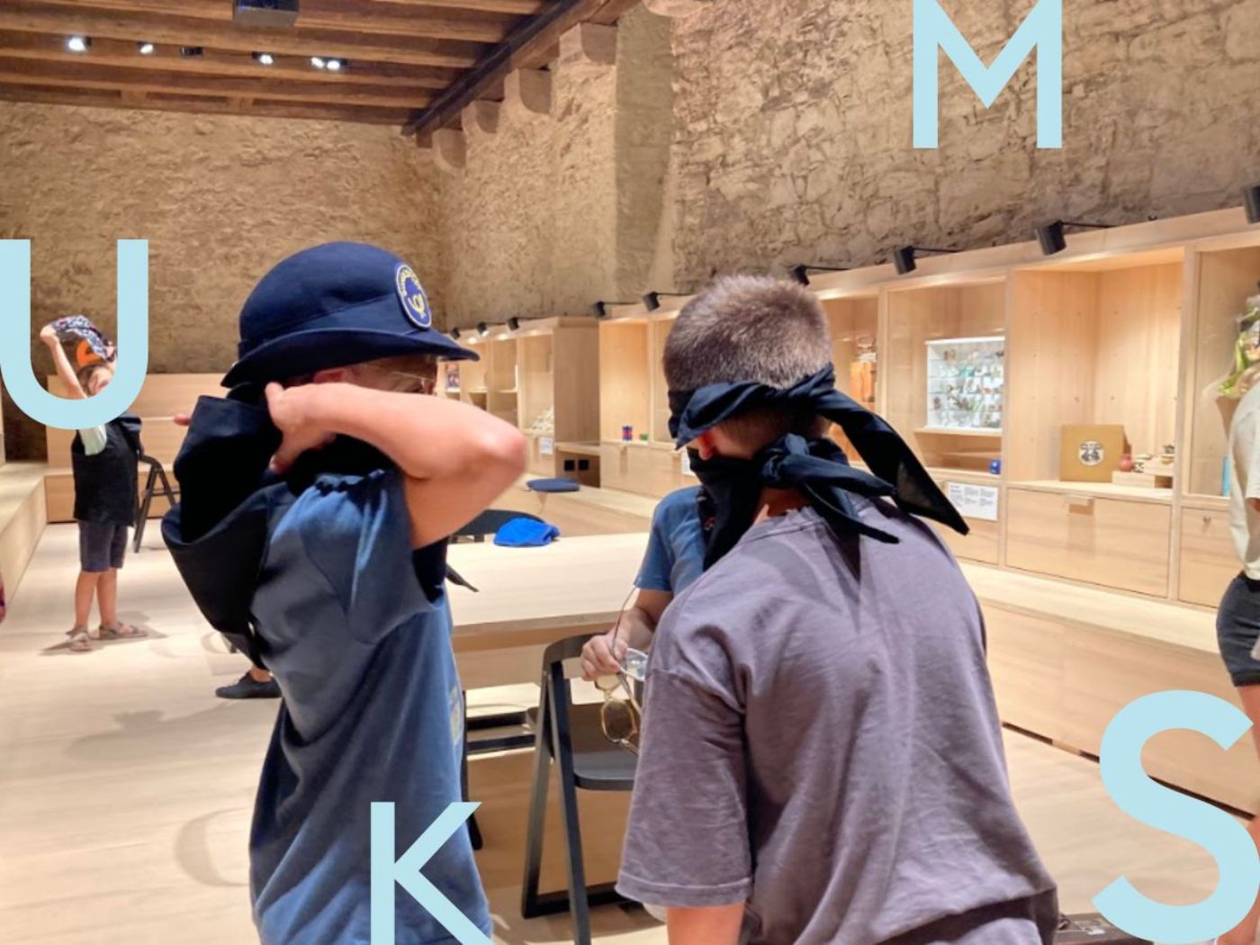 Auf einem Holztisch spielen drei Kinder mit verbundenen Augen in einem Raum mit Holzwänden