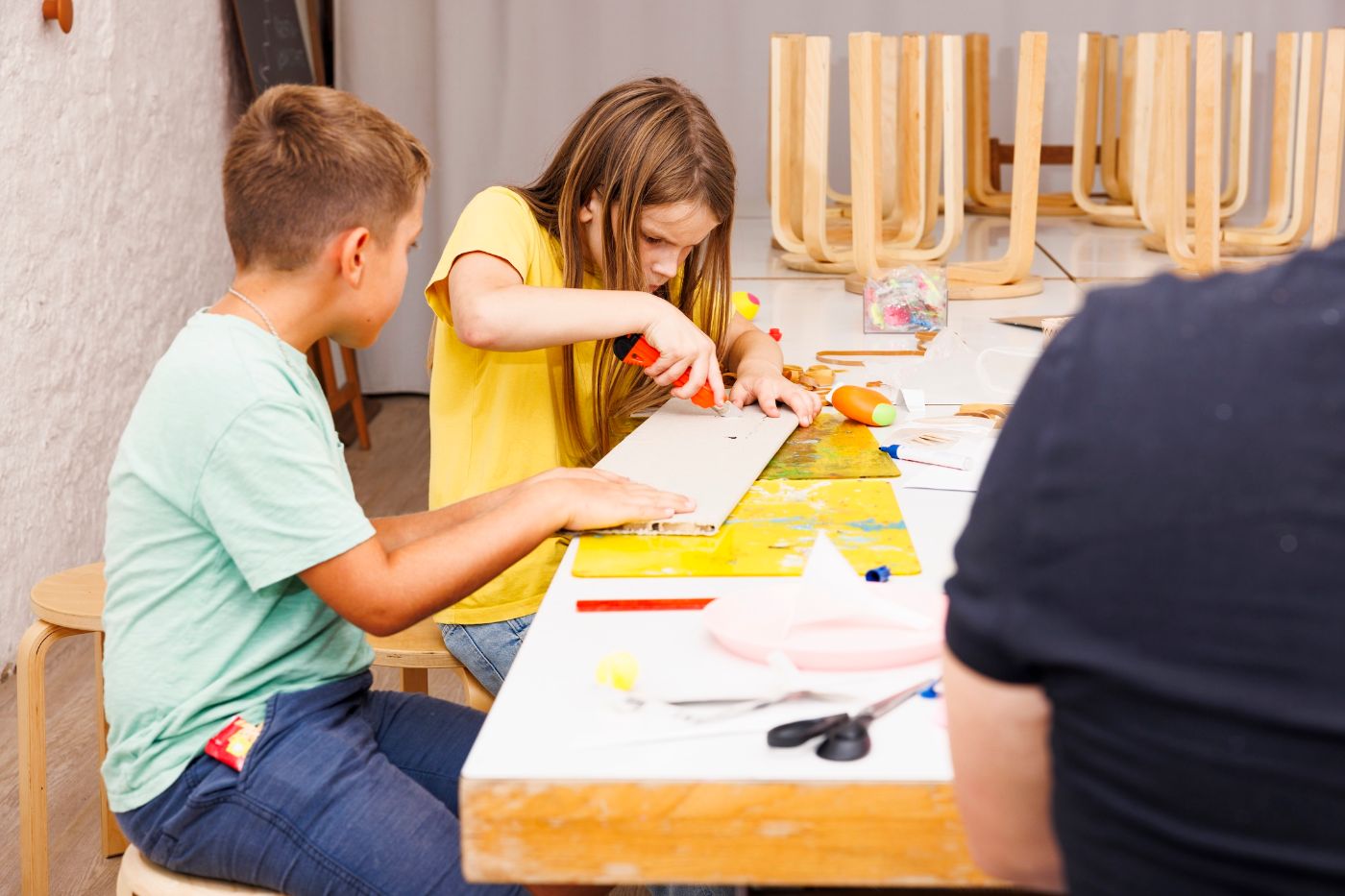 Auf einem Tisch basteln zwei Kinder konzentriert mit buntem Papier und Bastelwerkzeugen