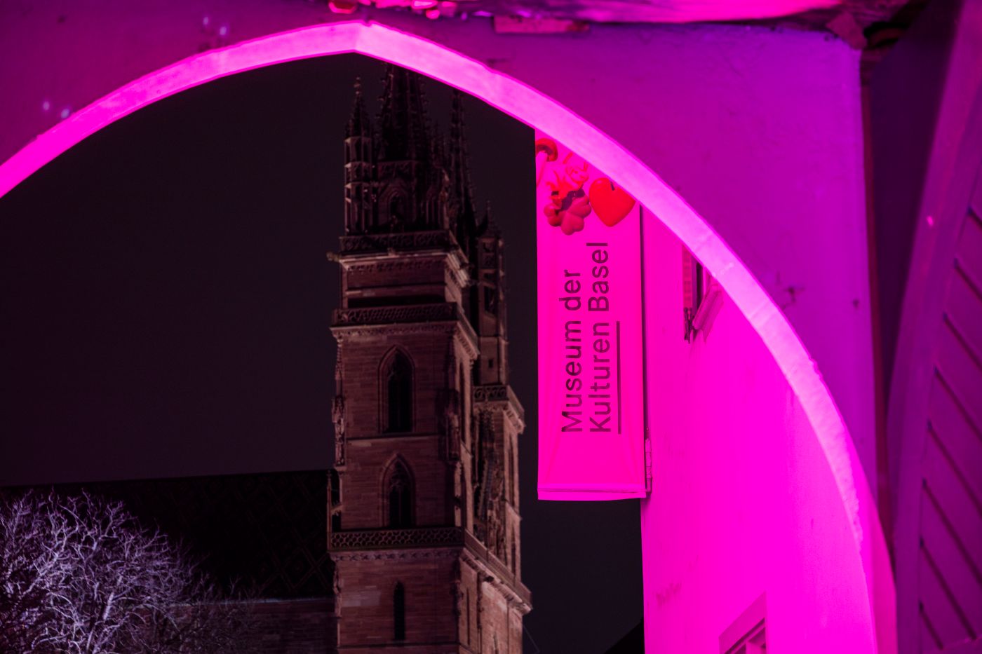 Eingangstor zum Museum, pink beleuchtet. Durch das Tor sieht man das Museumsbanner und das Basler Münster im Hintergrund.