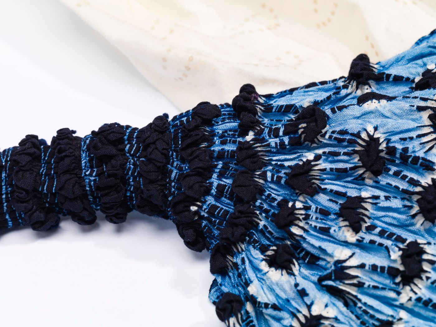 Ein blaues Textil im Shibori-Stil mit Knoten und Falten liegt auf weissem Stoff