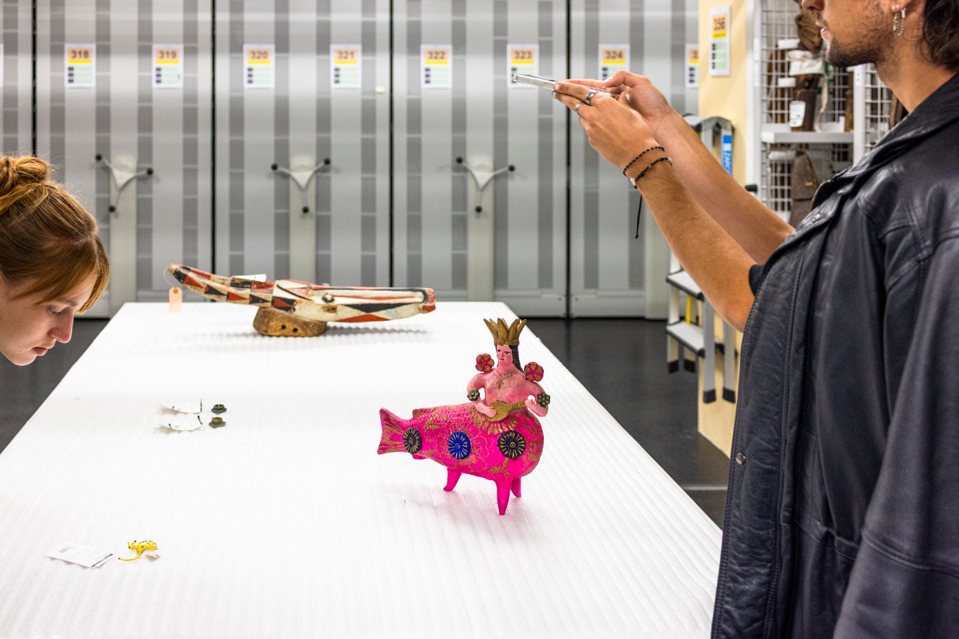 Eine pinke Meerjungfrauenfigur mit Krone wird auf einem Tisch betrachtet und fotografiert.