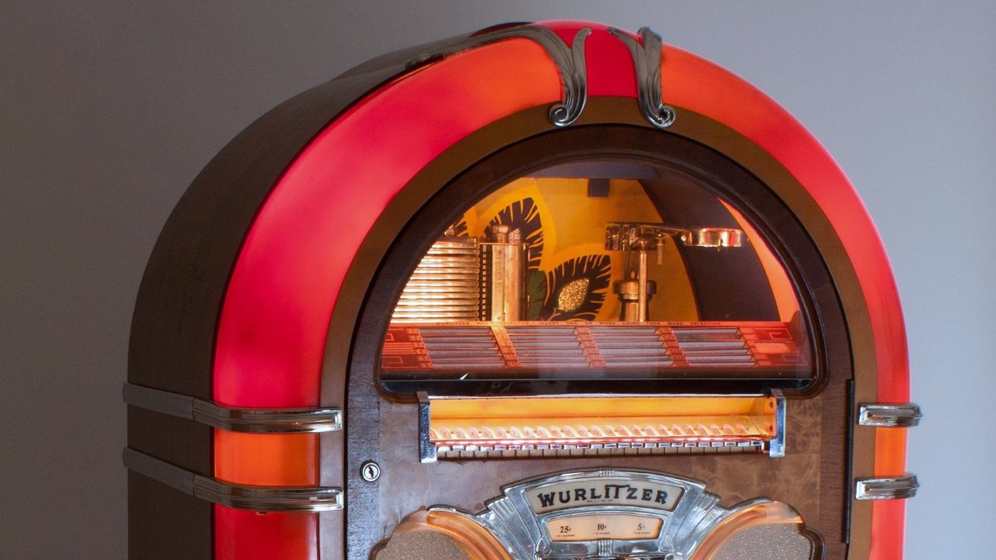 Ein alter Wurlitzer-Musikautomat mit beleuchteten Details steht gegen eine graue Wand