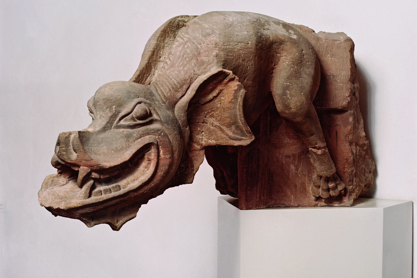 Ein lächelnder Wasserspeier aus Stein mit groteskem Gesicht und langen Ohren auf Podest.