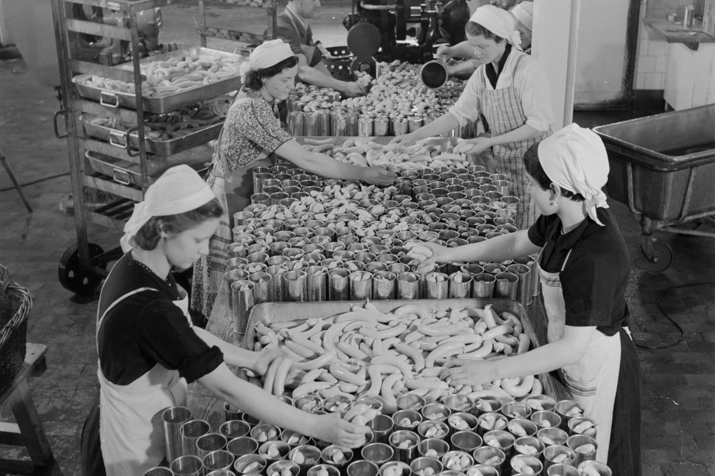 Arbeiterinnen und Arbeiter der Bell AG verpacken im Jahr 1939 Würste in Konservendosen.