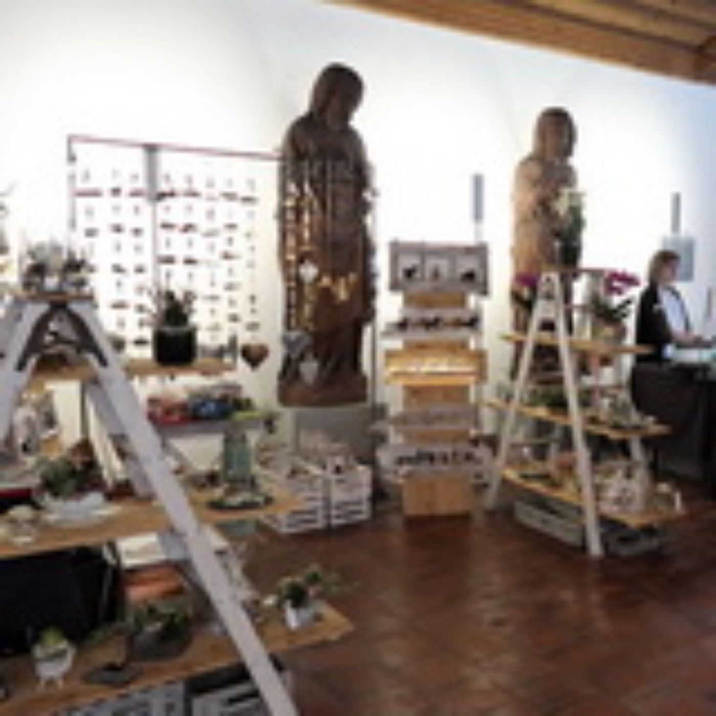 Zwei hölzerne Skulpturen zwischen Leiterregalen mit Kunsthandwerk auf einem Kunstmarkt