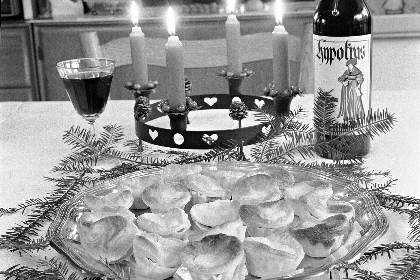 Ein adventlicher Tisch mit brennenden Kerzen, Gebäck, einem Glas Rotwein und einer Hypokrasflasche.