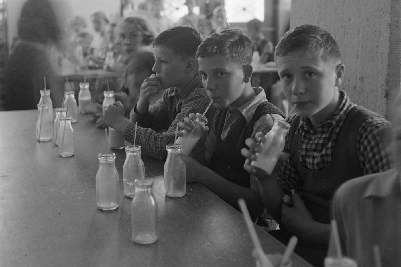 Schulkinder in Basel aus dem Jahr 1938 trinken Milch mit Strohhalmen aus Glasflaschen.