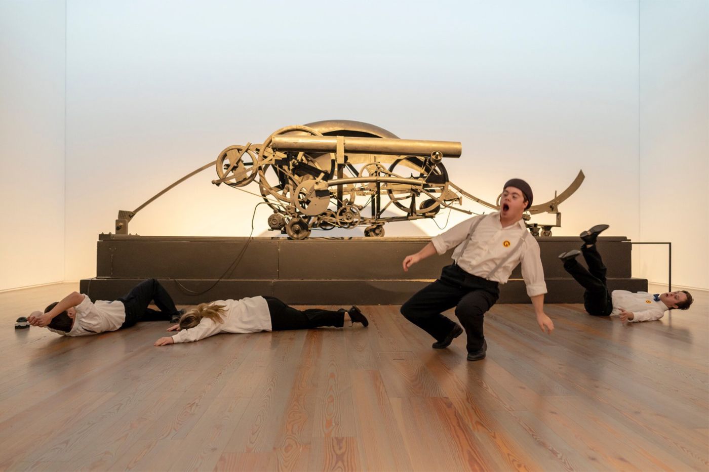 Vier Personen in weissen Hemden posieren dynamisch vor einer grossen, mechanischen Skulptur.