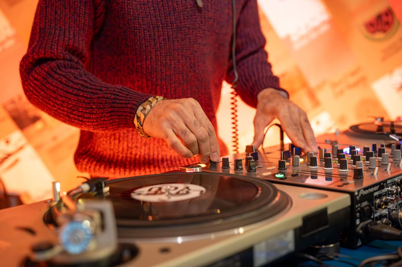 Ein DJ in rotem Pullover mixt Musik an einem Plattenteller und Mischpult