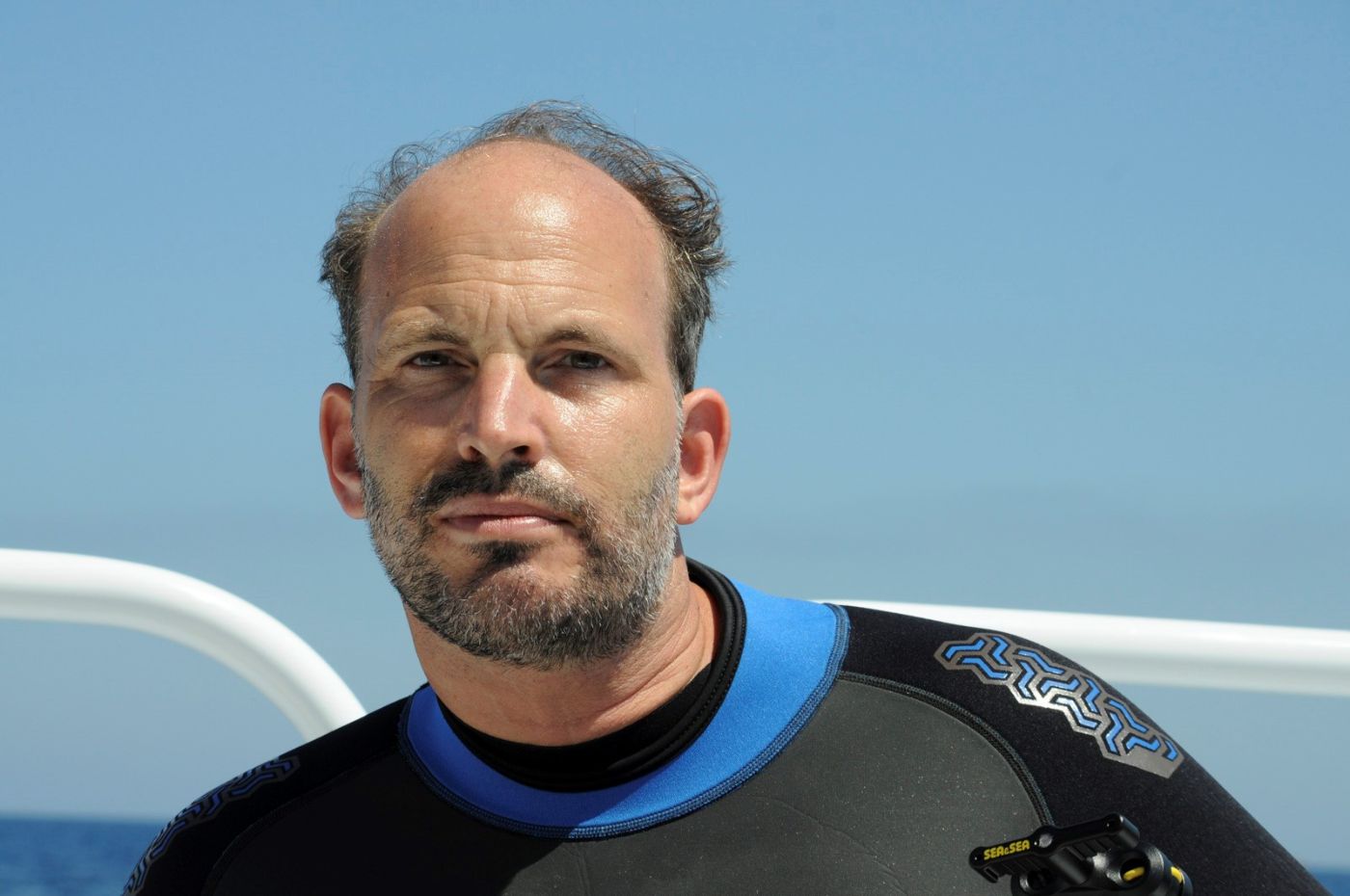 Prinz Hussain Aga Khan steht im Tauchanzug auf einem Boot im Meer.