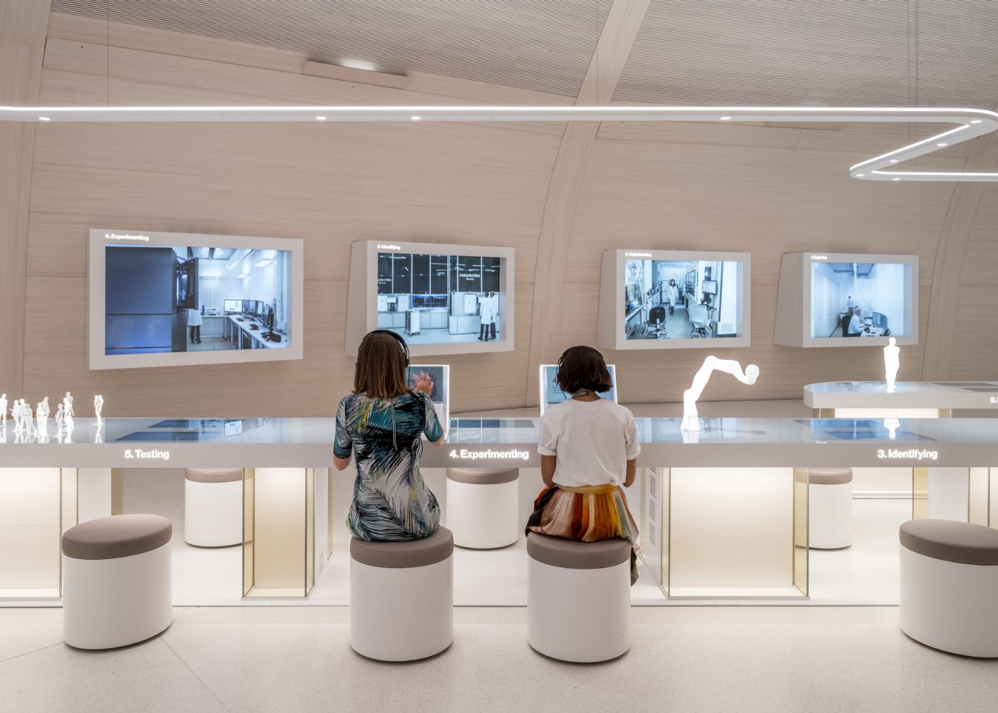 Two people sit at an interactive table, surrounded by screens showing laboratory images