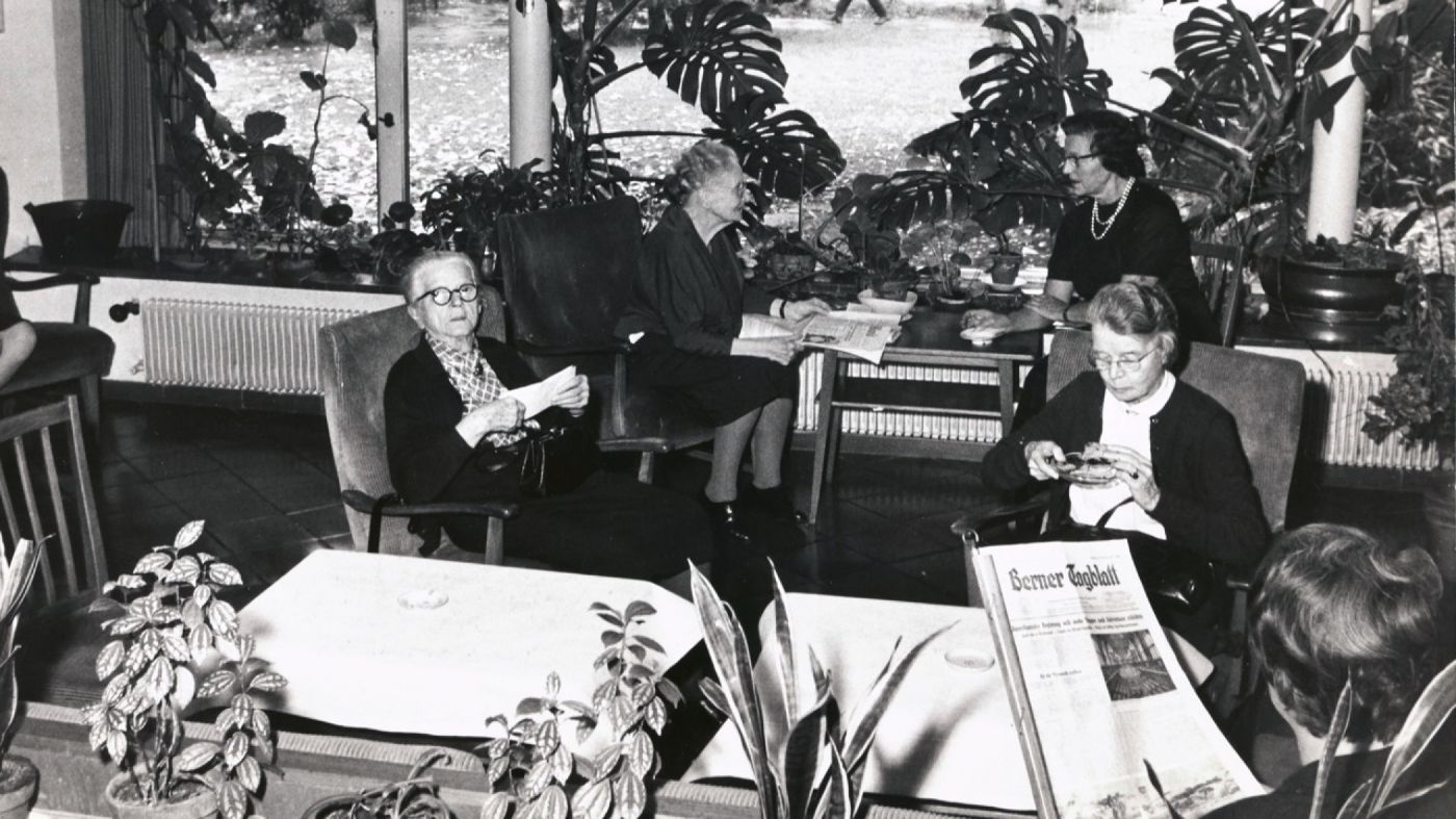 Ältere Frauen sitzen in einem Raum mit grossen Pflanzen, lesen und unterhalten sich