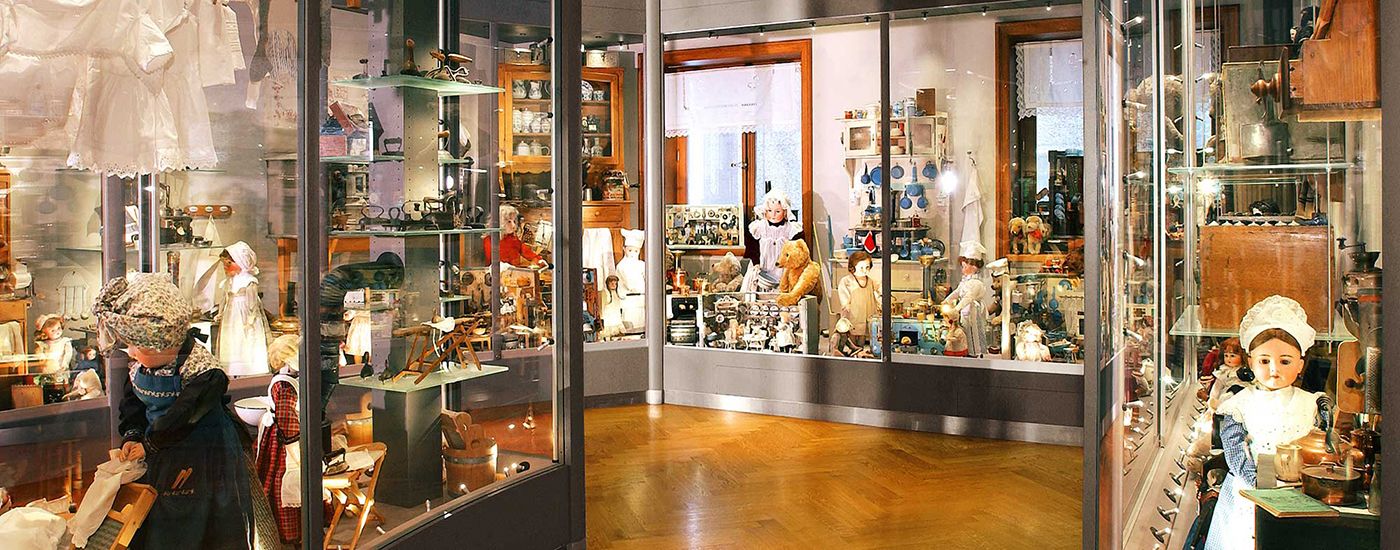 Dolls and teddy bears in glass cabinets, surrounded by miniatures and toys on wooden shelves