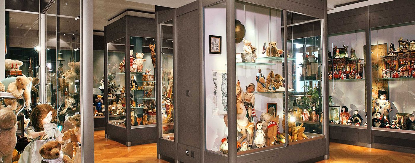 Teddy bears and dolls are displayed in glass cases, surrounded by toy landscapes.