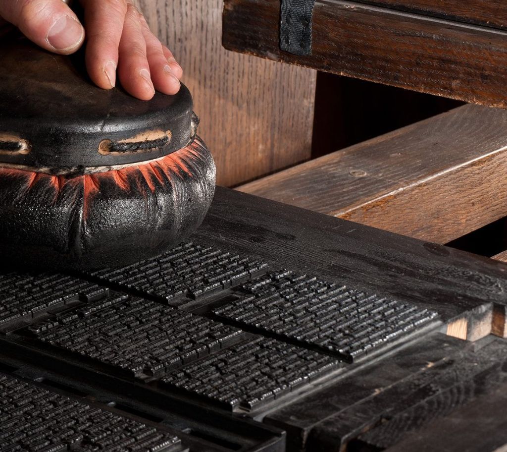 A leather dabber is used by a hand to polish black print letters on a wooden table