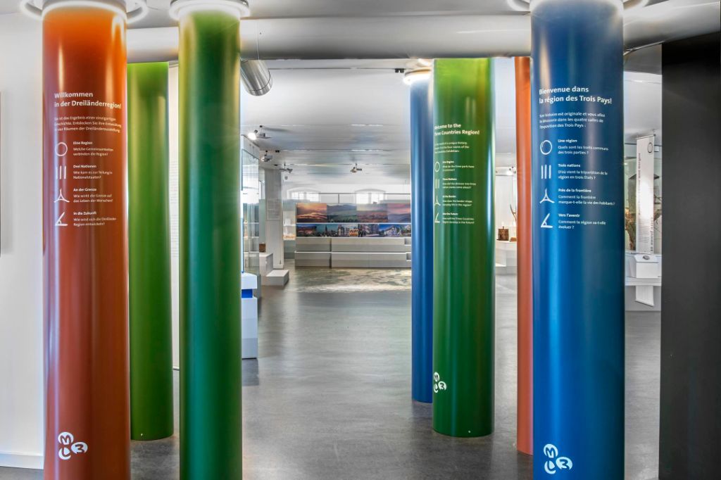 Kunterbunte Säulen mit mehrsprachigen Willkommensbotschaften stehen im Ausstellungsraum.