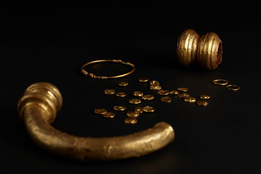 Goldene antike Schmuckstücke und Münzen liegen auf einer schwarzen Oberfläche ausgebreitet