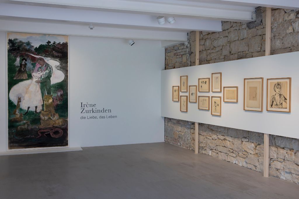 Ein grosses Gemälde und mehrere Skizzen in hellen Rahmen an einer Steinwand ausgestellt